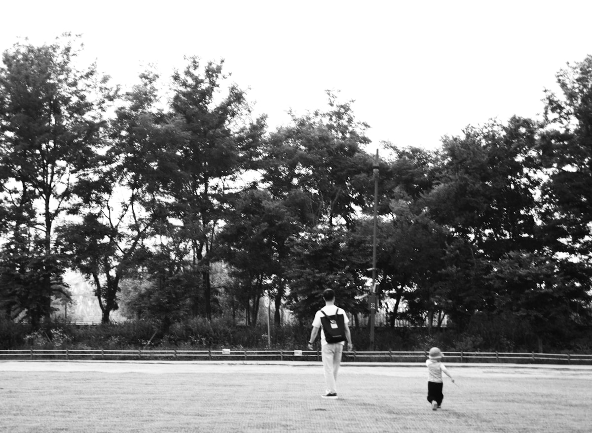 A parent and a small child walking together along a tree-lined path