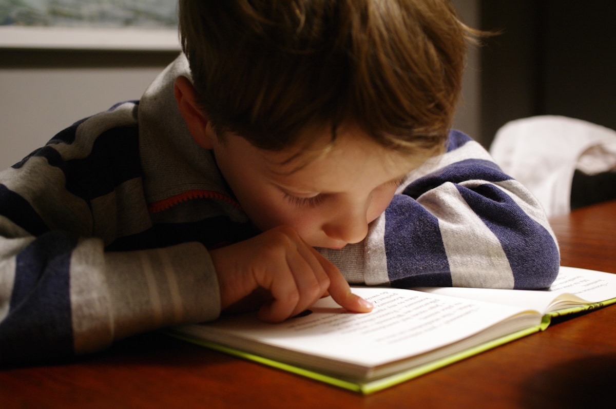 A young child following the words with their finger as they read a book
